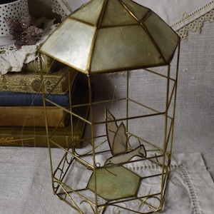 May include: A gold metal birdcage with a white and gold iridescent roof. The cage is empty except for a white bird with a gold beak and wings.