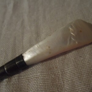 May include: A white mother-of-pearl handle with a silver metal shaft. The handle has a decorative pattern.