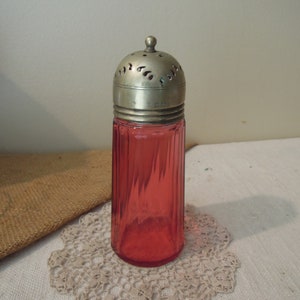 May include: A vintage glass sugar dispenser with a ribbed, pink glass body and a silver, pierced top.