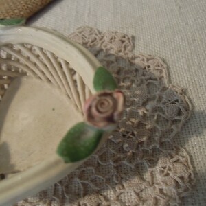 Puede incluir: Una cesta de cer&aacute;mica blanca con un dise&ntilde;o tejido y acentos de rosas rosas. La cesta tiene forma de coraz&oacute;n y tiene un dise&ntilde;o de hojas verdes.