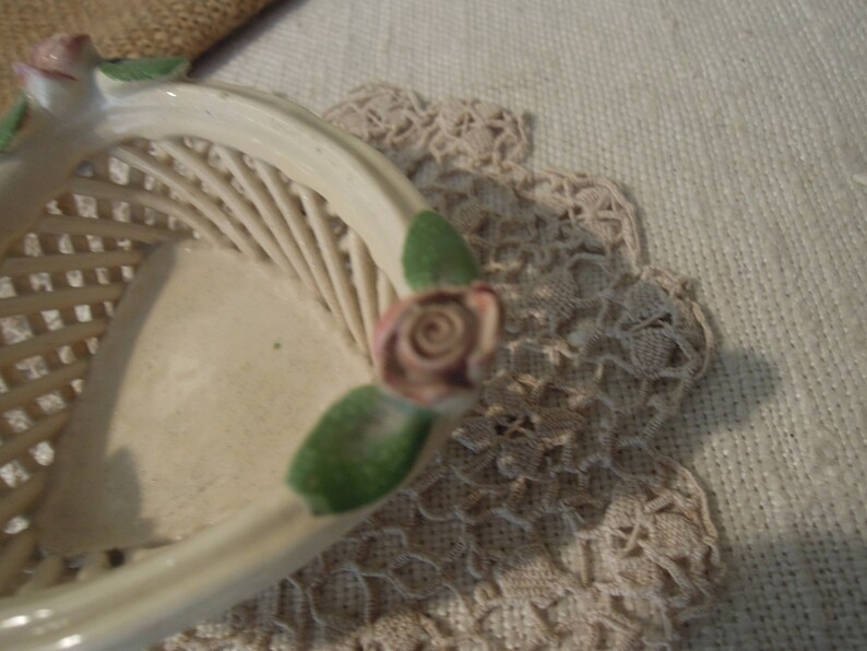 Puede incluir: Una cesta de cer&aacute;mica blanca con un dise&ntilde;o tejido y acentos de rosas rosas. La cesta tiene forma de coraz&oacute;n y tiene un dise&ntilde;o de hojas verdes.