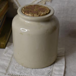 May include: A white ceramic jar with a cork lid. The jar is sitting on a white doily.