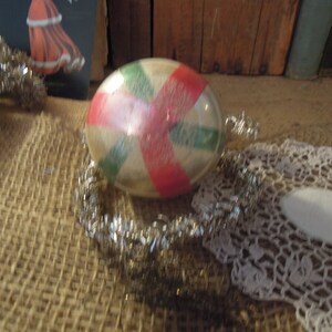 May include: A vintage glass Christmas ornament with a red, white, and green candy cane design. The ornament is round and has a shiny, reflective surface.