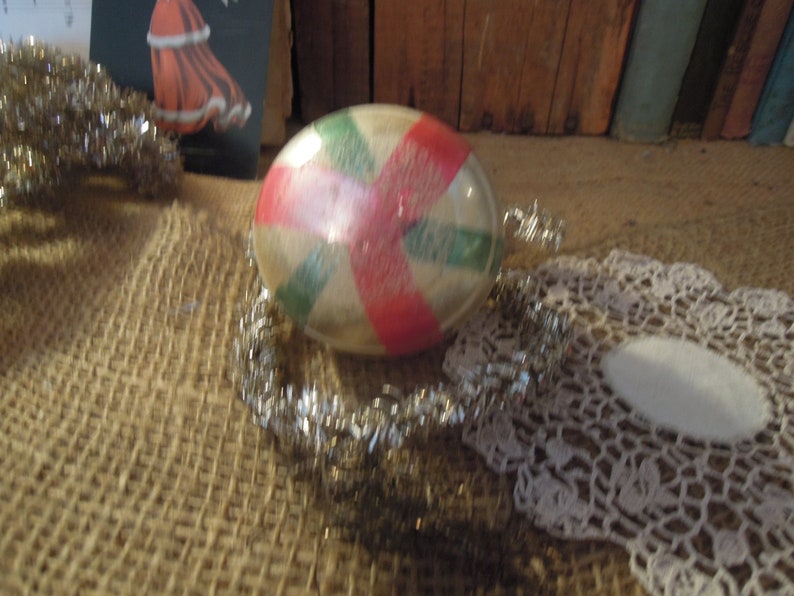 May include: A vintage glass Christmas ornament with a red, white, and green candy cane design. The ornament is round and has a shiny, reflective surface.