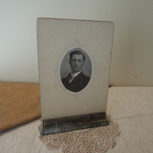 May include: A vintage photo frame with a black and white photo of a man wearing a suit and tie. The frame is made of metal and has a decorative design.