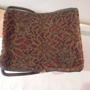 May include: A small, folding stool with a brown and red patterned fabric seat. The stool has a metal frame.