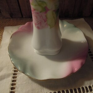 May include: A white porcelain ring holder with a scalloped edge and a floral design. The holder has a pink, green, and blue glaze.