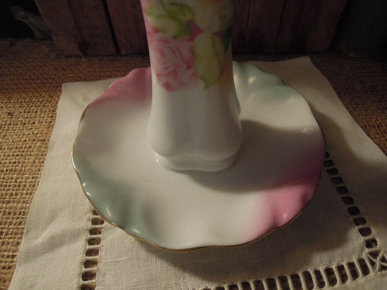May include: A white porcelain ring holder with a scalloped edge and a floral design. The holder has a pink, green, and blue glaze.