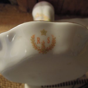 May include: A white porcelain dish with a scalloped edge and a floral design. The dish has the initials "R & S" in the centre.
