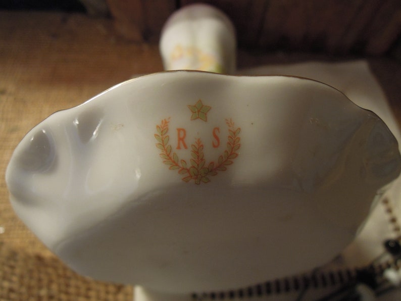 May include: A white porcelain dish with a scalloped edge and a floral design. The dish has the initials "R & S" in the centre.