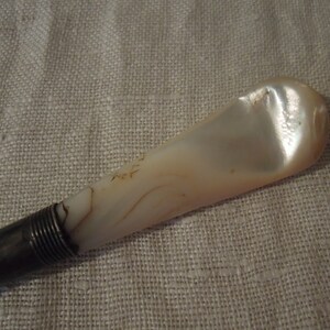 May include: A silver and mother-of-pearl shoe horn. The horn is a light cream color with brown swirls. The silver handle is ribbed.
