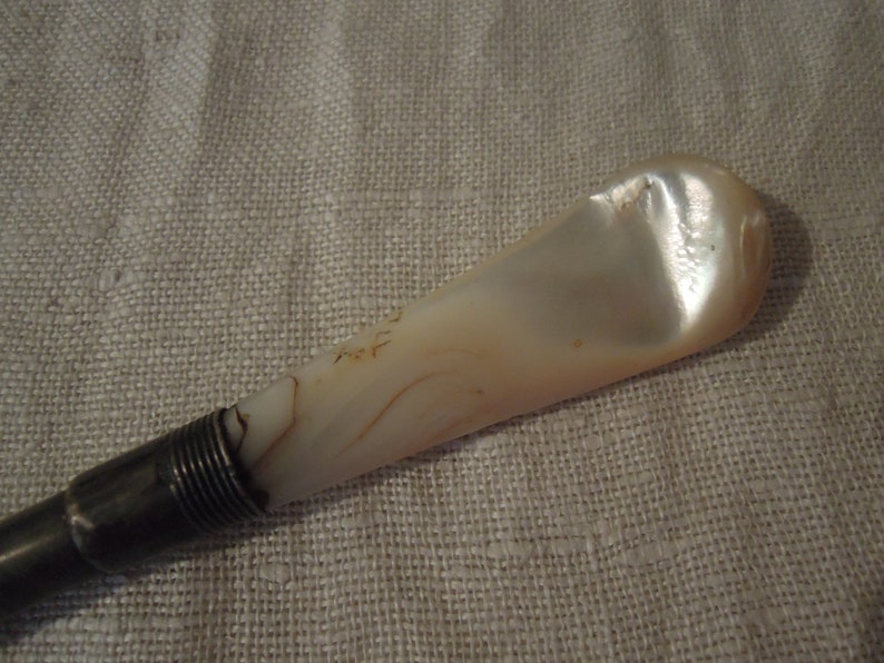 May include: A silver and mother-of-pearl shoe horn. The horn is a light cream color with brown swirls. The silver handle is ribbed.