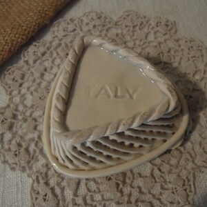 Puede incluir: Un plato de cer&aacute;mica blanca con un dise&ntilde;o de cuerda alrededor del borde. El plato tiene forma de tri&aacute;ngulo y tiene un fondo texturizado elevado. La palabra "ITALIA" est&aacute; grabada en relieve en el plato.