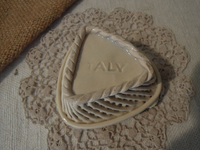 Puede incluir: Un plato de cer&aacute;mica blanca con un dise&ntilde;o de cuerda alrededor del borde. El plato tiene forma de tri&aacute;ngulo y tiene un fondo texturizado elevado. La palabra "ITALIA" est&aacute; grabada en relieve en el plato.