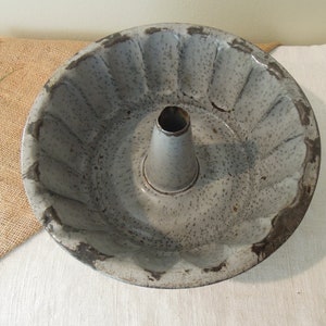 Könnte beinhalten: Eine vintage graue Metall-Bundtkuchenform mit geriffeltem Rand und einem zentralen Rohr. Die Form hat eine gesprenkelte graue Oberfläche und weist Gebrauchsspuren auf.