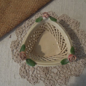 Puede incluir: Una cesta triangular de cer&aacute;mica blanca con un dise&ntilde;o tejido y tres rosas rosas en el borde.