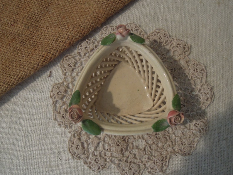 Puede incluir: Una cesta triangular de cer&aacute;mica blanca con un dise&ntilde;o tejido y tres rosas rosas en el borde.