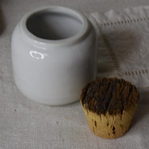 May include: White ceramic jar with a cork lid. The lid is made of dark brown cork.