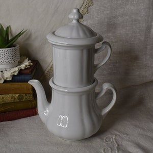 May include: White porcelain coffee pot with a separate filter and lid. The pot has a fluted design and a classic shape.