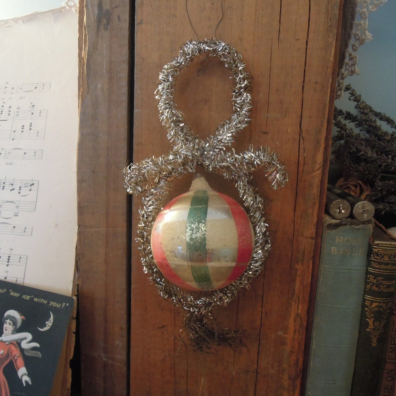 May include: A vintage Christmas ornament with a silver tinsel hanger and a glass ball with red, green, and white stripes.