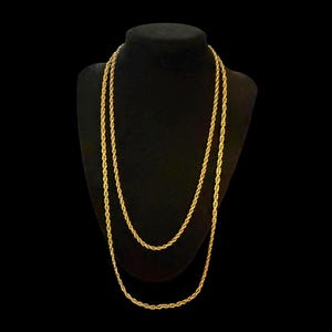 May include: A long gold-toned rope chain necklace featuring a twisted metal link design. The necklace is displayed as a double-layered strand, showcasing the continuous, uniform texture of the metallic rope links throughout the entire length.