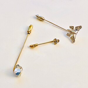 May include: Three decorative pins in gold and silver. One pin features a clear crystal, one has a cluster of small crystals, and the third is a silver butterfly with crystal accents.