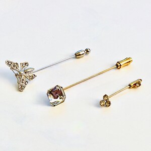 May include: Three decorative pins with different embellishments. The first pin has a silver butterfly design, the second pin has a clear square crystal, and the third pin has three small clear crystals.