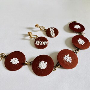 Peut inclure: Un ensemble de boucles d'oreilles et d'un bracelet marron et blanc. Les boucles d'oreilles et le bracelet sont en m&eacute;tal et pr&eacute;sentent un motif blanc sur fond marron.