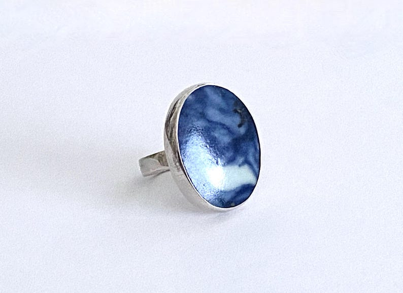 May include: A silver ring with a blue and white enamel inlay. The inlay has a swirling pattern.