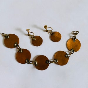 Peut inclure: Un ensemble de boucles d'oreilles dor&eacute;es et un bracelet avec des disques ronds en cuivre reli&eacute;s par une cha&icirc;ne.