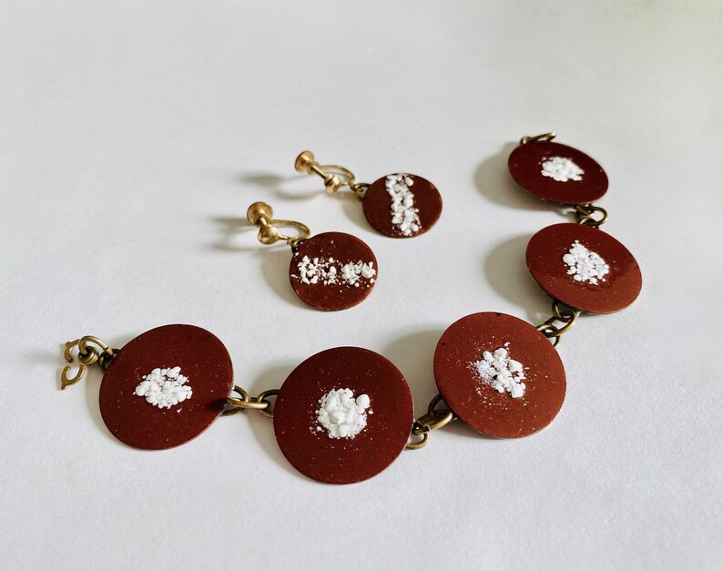 Peut inclure: Un ensemble de boucles d'oreilles et d'un bracelet marron et blanc. Les boucles d'oreilles et le bracelet sont en m&eacute;tal et pr&eacute;sentent un motif blanc sur fond marron.