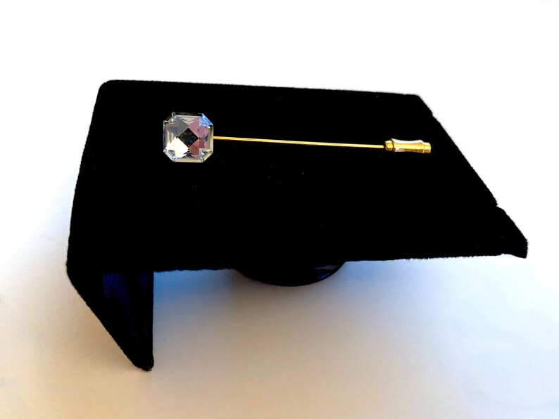 May include: A gold tie tack with a clear, faceted, square-shaped crystal.