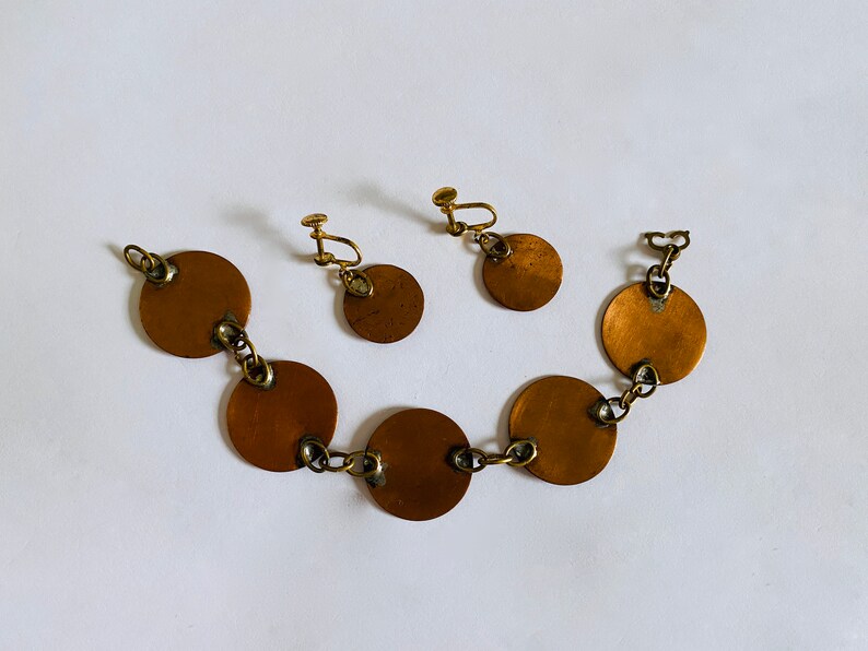 Peut inclure: Un ensemble de boucles d'oreilles dor&eacute;es et un bracelet avec des disques ronds en cuivre reli&eacute;s par une cha&icirc;ne.