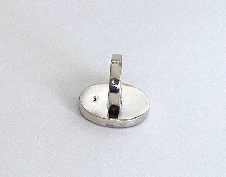 May include: A silver ring with a smooth oval-shaped setting. The ring is shown from the back, revealing the smooth band and the setting.