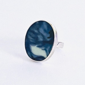 May include: A silver ring with a blue and white oval-shaped resin inlay. The resin has a marbled pattern.