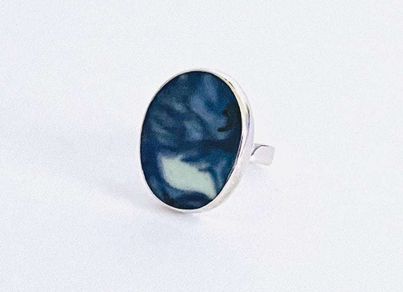 May include: A silver ring with a blue and white oval-shaped resin inlay. The resin has a marbled pattern.