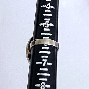 May include: A silver ring with a black and white stone set in the center. The ring is shown on a ruler, measuring approximately size 7.