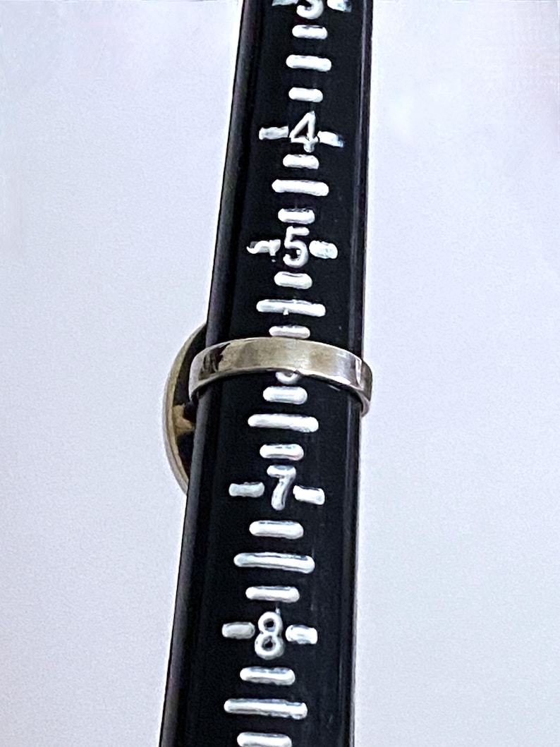 May include: A silver ring with a black and white stone set in the center. The ring is shown on a ruler, measuring approximately size 7.