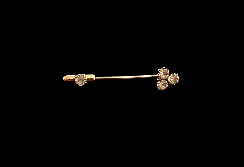 May include: A gold-toned safety pin with three clear rhinestones at the end.