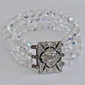 May include: A multi-strand crystal bracelet with a silver-toned clasp featuring a square-shaped rhinestone in the center.