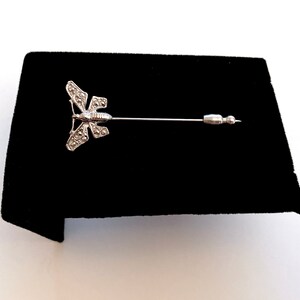 May include: A silver butterfly brooch with a pin. The butterfly has a detailed design with small stones.