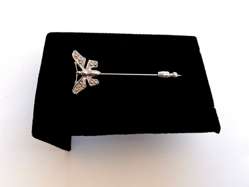 May include: A silver butterfly brooch with a pin. The butterfly has a detailed design with small stones.