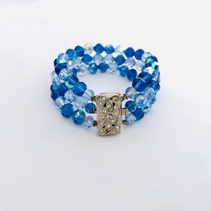 May include: A blue and clear crystal beaded bracelet with a silver clasp. The bracelet is made of multiple strands of beads.