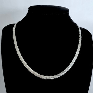 May include: A silver chain necklace with a twisted design. The necklace is displayed on a black velvet stand.