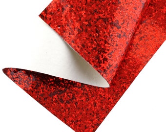 Op de afbeelding: Close-up van een vel rode glitterstof met een witte achterkant. De stof is dubbelgevouwen, waardoor de witte onderkant zichtbaar is. De rode glitter is dicht op elkaar gepakt, wat een sprankelend effect creëert.