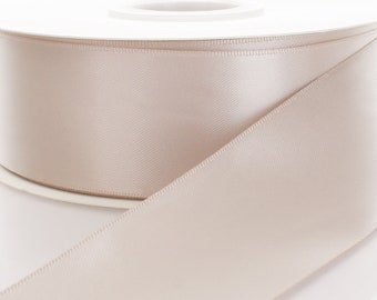 May include: A spool of light beige satin ribbon. The ribbon is wound around a white spool.