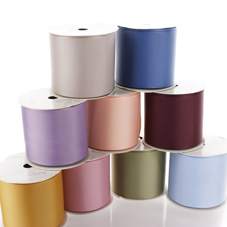 May include: A collection of eight spools of ribbon in various colors, including light blue, lavender, beige, peach, burgundy, green, and light pink. The spools are arranged in a pyramid shape.