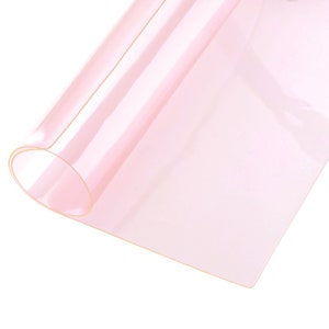 May include: A rolled sheet of translucent, pale pink material. The material appears thin and flexible, with a slight sheen. The edges of the sheet are visible, showing a rolled-up section.