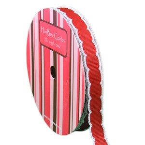 Op de afbeelding: Rood en wit lint met een gegolfde rand. Het lint zit op een spoel met een roze en bruin gestreept etiket waarop "HairBow Center" en "The supply store" staat.