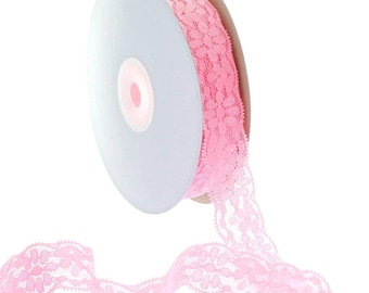 May include: A spool of pink lace ribbon with a floral pattern. The ribbon is wound around a white cardboard spool.
